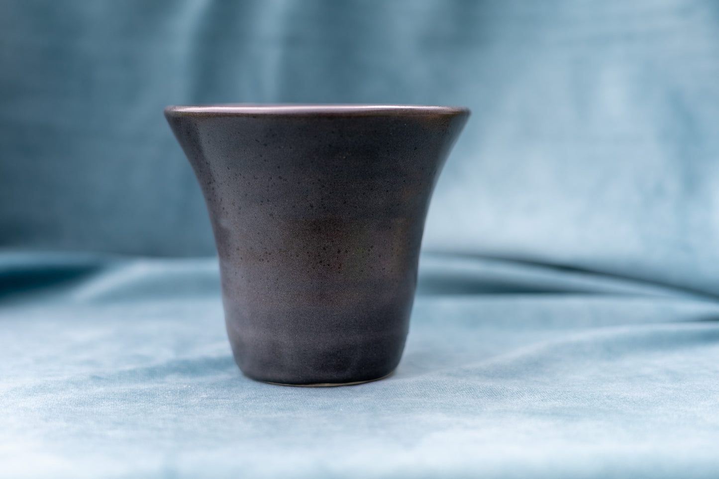 Charcoal ceramic cup on a textured light blue surface with a blurred blue background