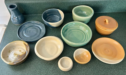 A collection of pottery including bowls and vases that are blue, caramel, and mint colours. 